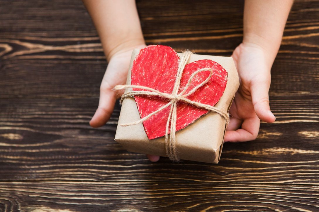 Kinderhände überreichen Geschenk mit rotem Herz aus Papier 