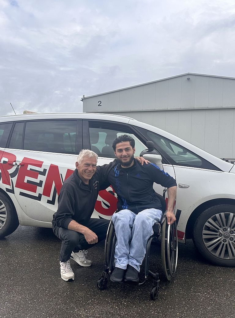 Fahrlehrer und junger Mann im Rollstuhl vor Auto