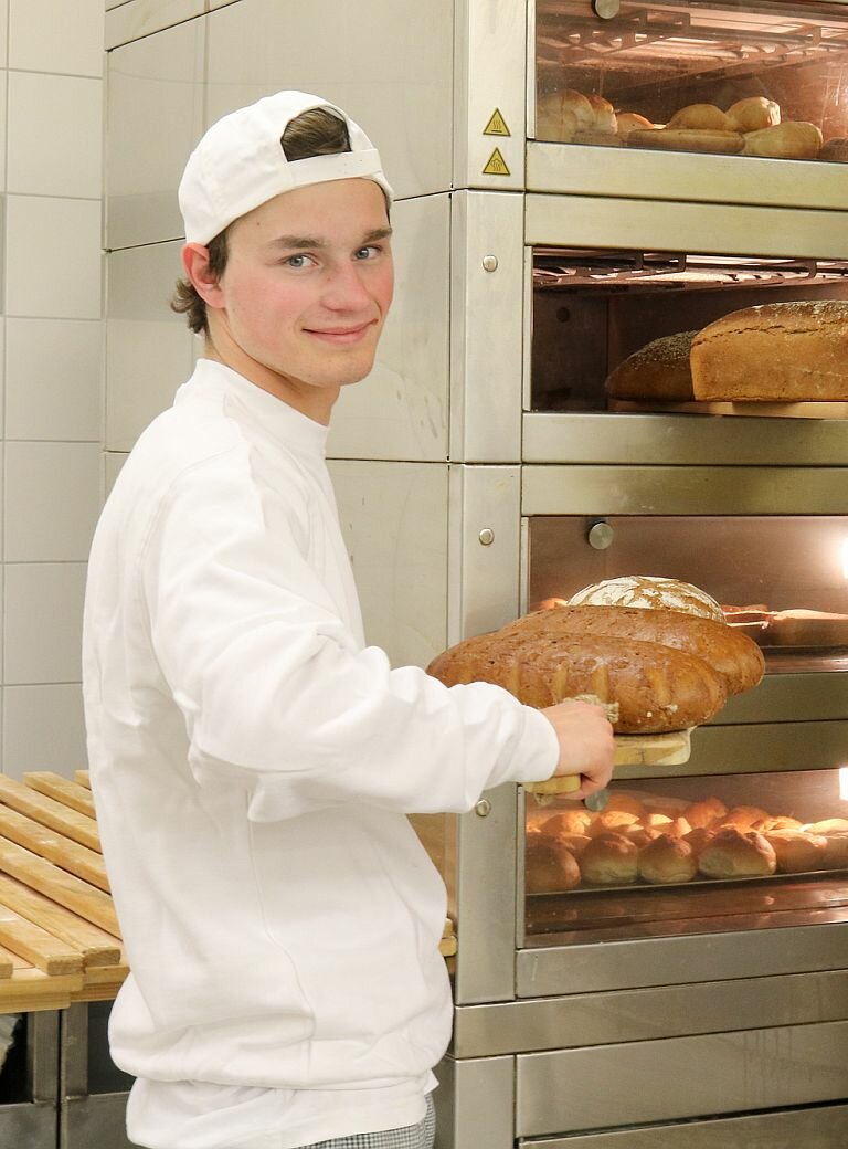 Zwei junge Männer in Bäckerkleidung mit Broten vor Ofen