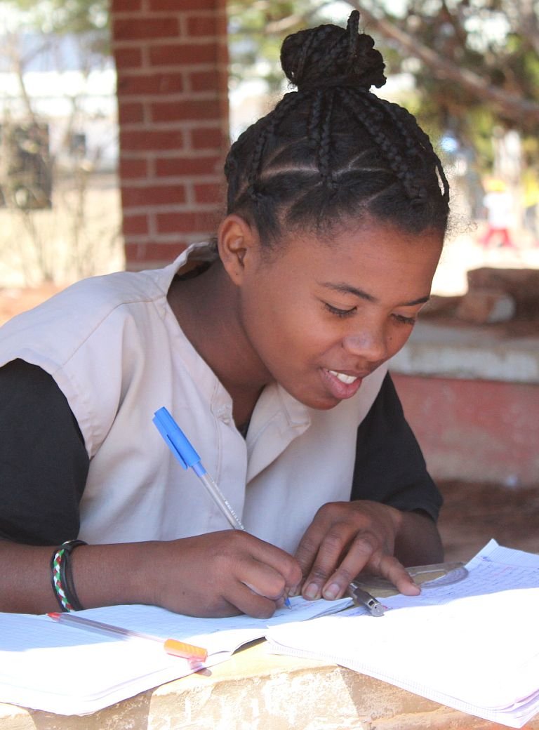 Junge Frau sitzt in Don Bosco Zentraum in Fianarantsoa in Madagaskar an Schulbank und schreibt in ihr Heft 