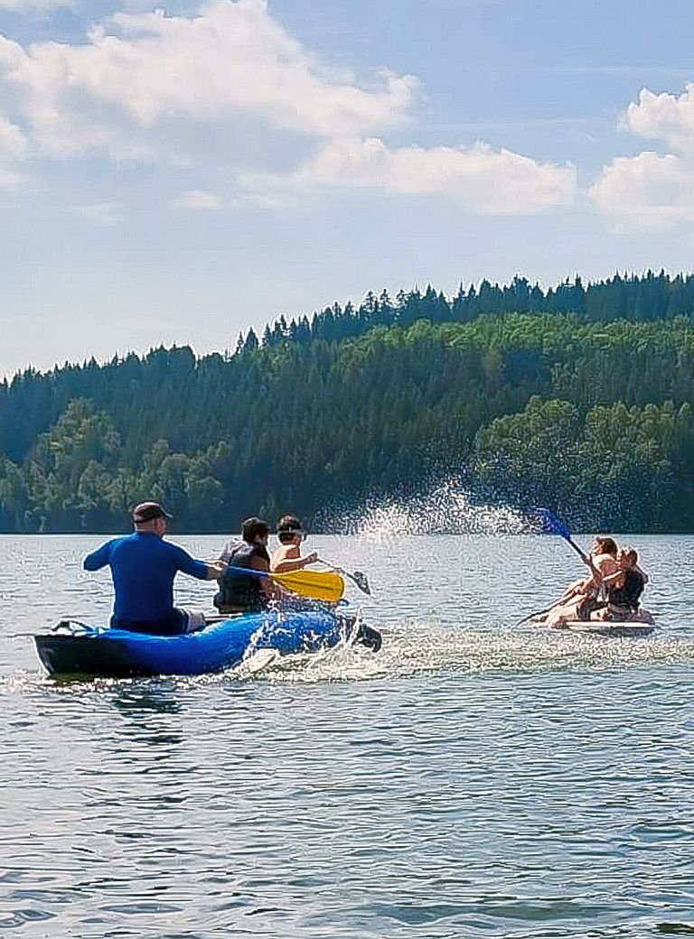 Jugendliche und Betreuer in Booten auf See vor Wald 