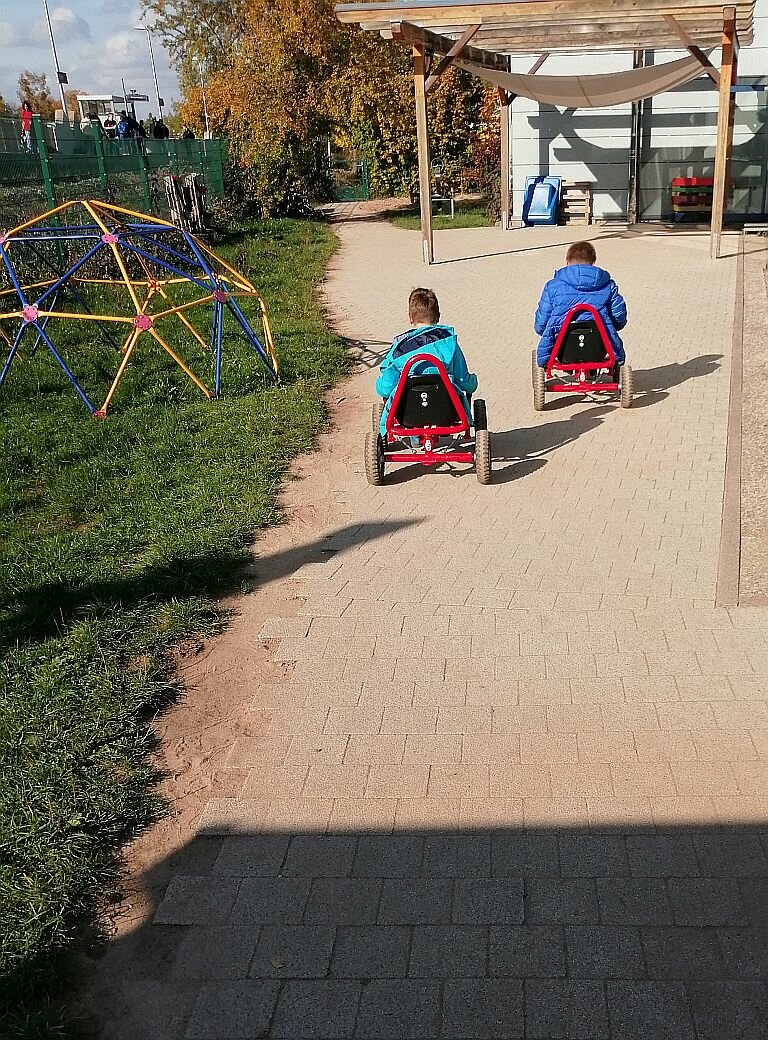Zwei Kinder fahren auf großen stabilen Fahrzeugen auf dem Außengelände der Tagesstätte Ebern 