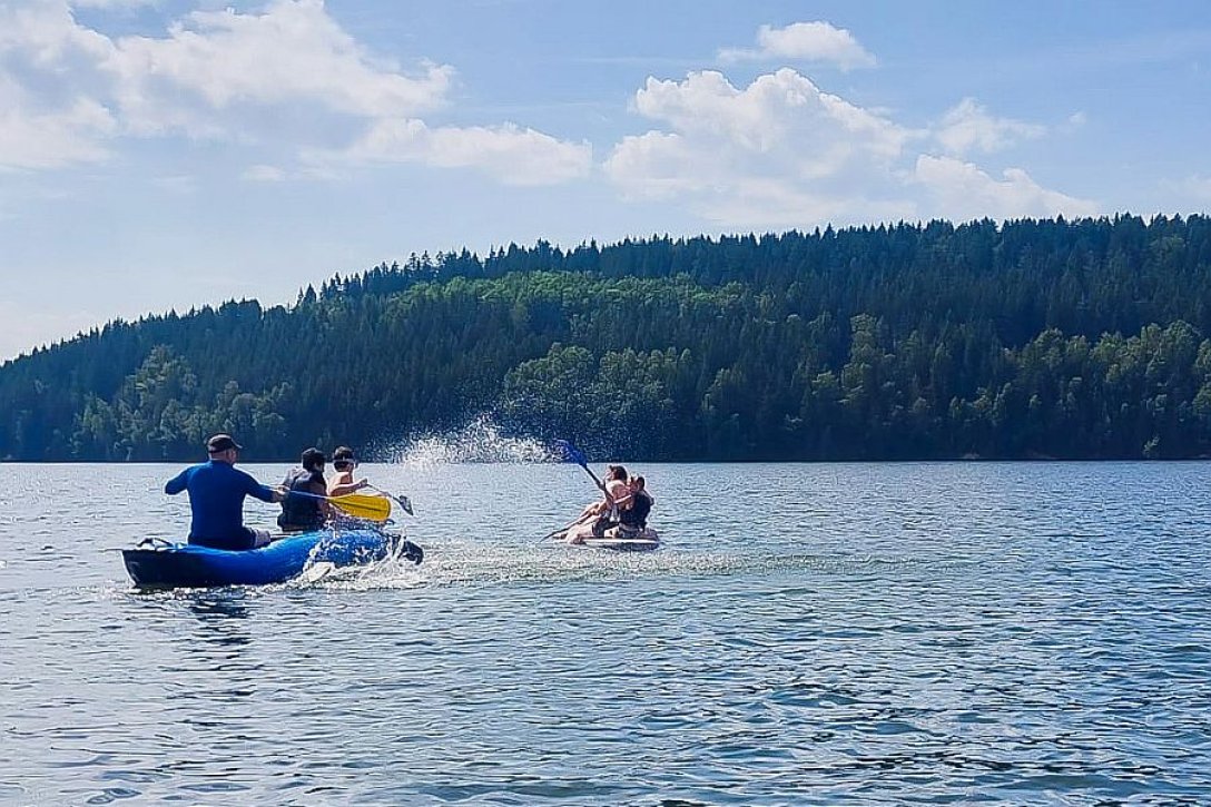 Jugendliche und Betreuer in Booten auf See vor Wald