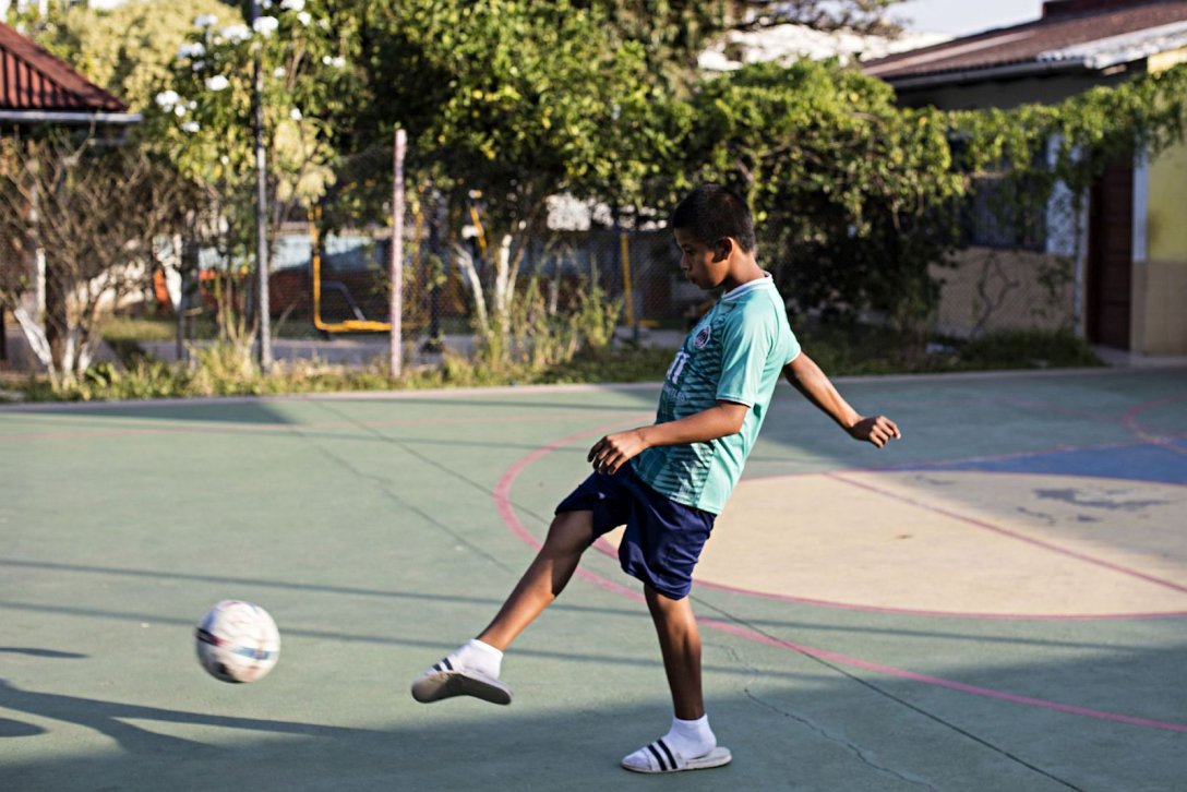 Jugendlicher kickt Fußball auf Sportplatz bei Don Bosco in Santa Cruz
