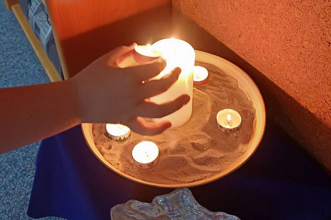 Kinderhand zündet Teelicht an großer weißer Kerze an, daneben in einer Schale weitere brennende Teelichte