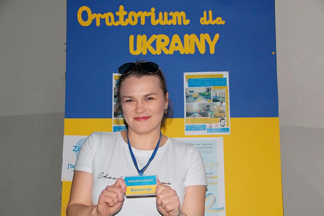 Frau steht vor blau-gelber Wand und zeigt Ausweiskarte in ukrainischen Nationalfarben 