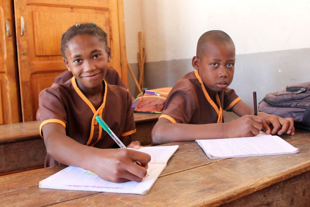 Kinder mit Heften auf einer Schulbank im Don Bosco Zentrum in Fianarantsoa