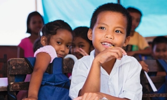 Kinder im Grundschulalter sitzen fröhlich in Klassenraum und lernen 