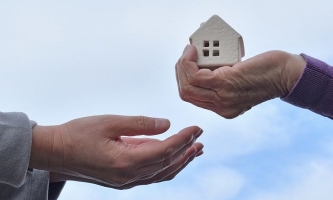 Hand gibt Modellhaus als Erbe oder Vermächtnis in andere Hände